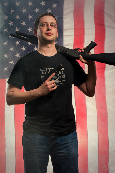 Portrait 2 from the An American Christmas series, person posing with a handgun in front of an American flag backdrop