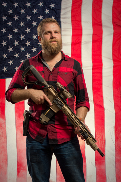 Portrait 4 from the An American Christmas series, person posing with a hunting rifle in front of an American flag backdrop