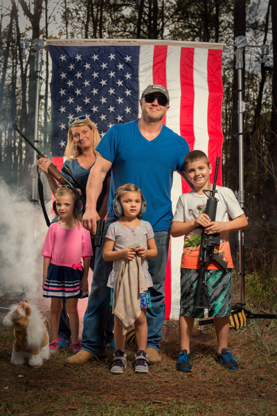 Portrait 6 from the An American Christmas series, person posing with a revolver in front of an American flag backdrop