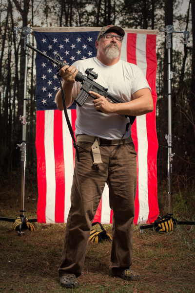 Portrait 8 from the An American Christmas series, person posing with a handgun in front of an American flag backdrop