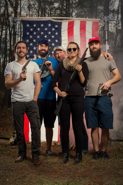 Portrait 9 from the An American Christmas series, person posing with a shotgun in front of an American flag backdrop