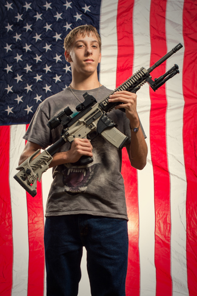 Portrait 11 from the An American Christmas series, person posing with an AR-style rifle in front of an American flag backdrop