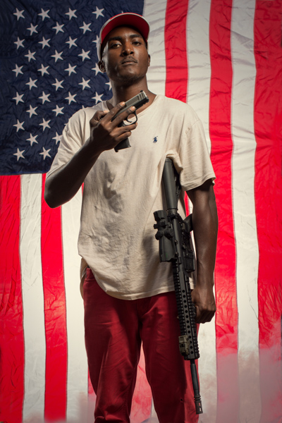 Portrait 12 from the An American Christmas series, person posing with a revolver in front of an American flag backdrop