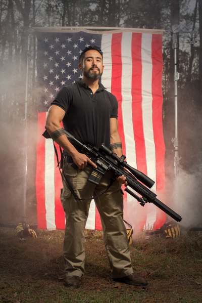 Portrait 15 from the An American Christmas series, person posing with a shotgun in front of an American flag backdrop