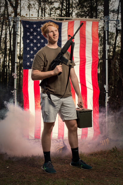 Portrait 17 from the An American Christmas series, person posing with an AR-style rifle in front of an American flag backdrop