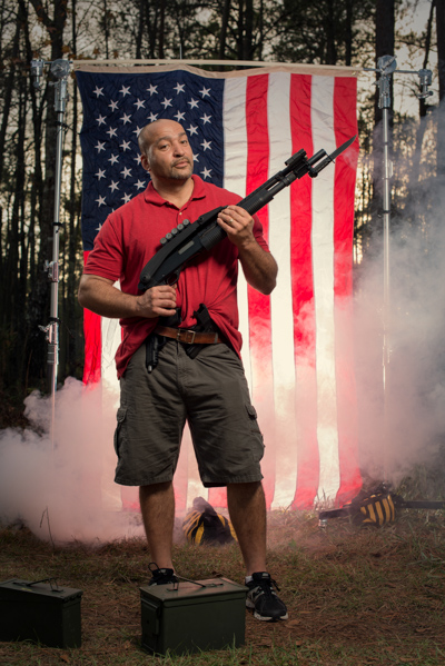Portrait 18 from the An American Christmas series, person posing with a revolver in front of an American flag backdrop