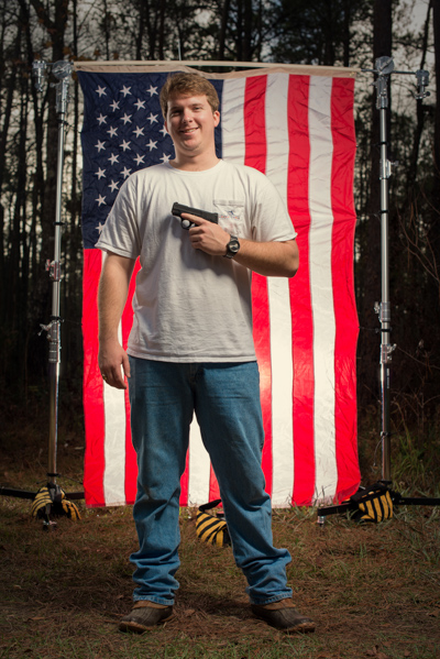Portrait 20 from the An American Christmas series, person posing with a handgun in front of an American flag backdrop