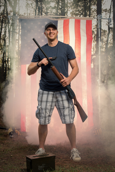 Portrait 22 from the An American Christmas series, person posing with a hunting rifle in front of an American flag backdrop