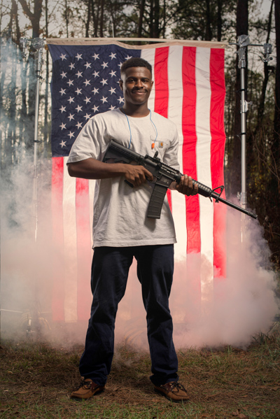 Portrait 24 from the An American Christmas series, person posing with a revolver in front of an American flag backdrop