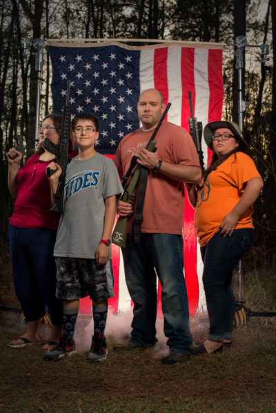 Portrait 26 from the An American Christmas series, person posing with a handgun in front of an American flag backdrop