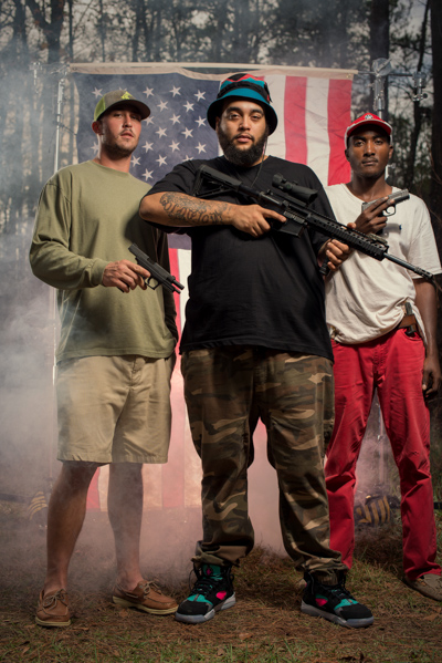 Portrait 27 from the An American Christmas series, person posing with a shotgun in front of an American flag backdrop