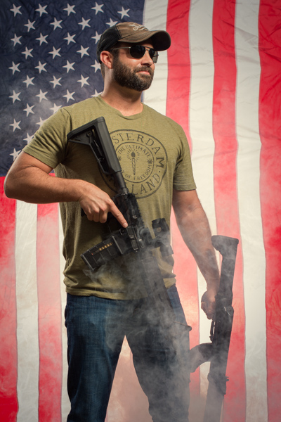 Portrait 30 from the An American Christmas series, person posing with a revolver in front of an American flag backdrop