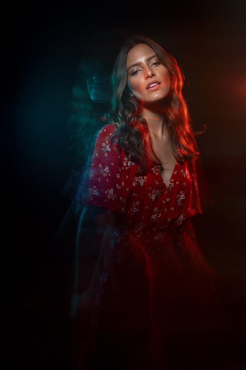 Woman lit in red and purple tones, looking down, artistic portrait