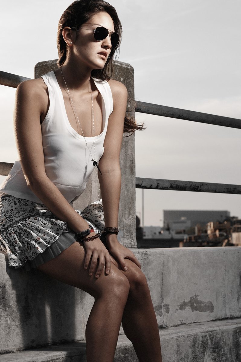 Woman in sunglasses and a sequined mini skirt sitting on a rooftop ledge