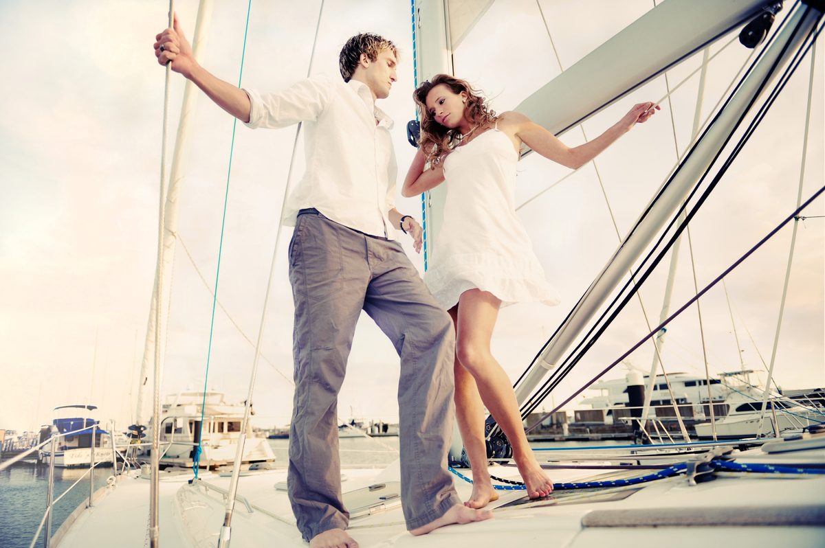 Man and woman posing together on the deck of a sailboat at a marina