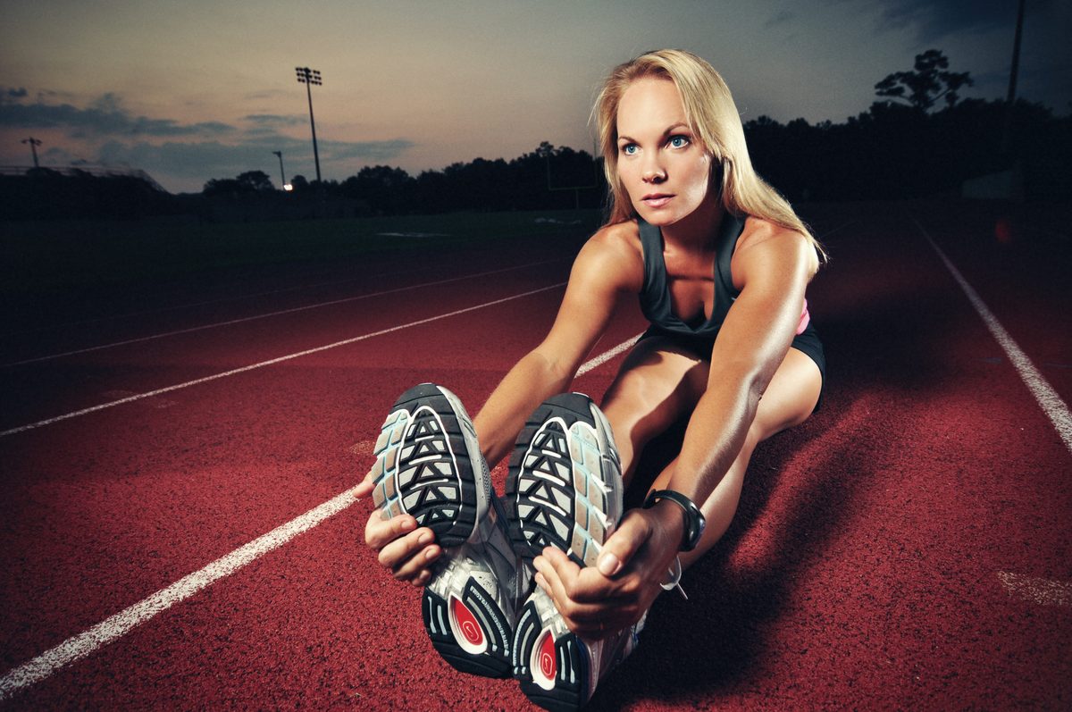 Woman stretching on a running track at dusk, athletic wear and sneakers
