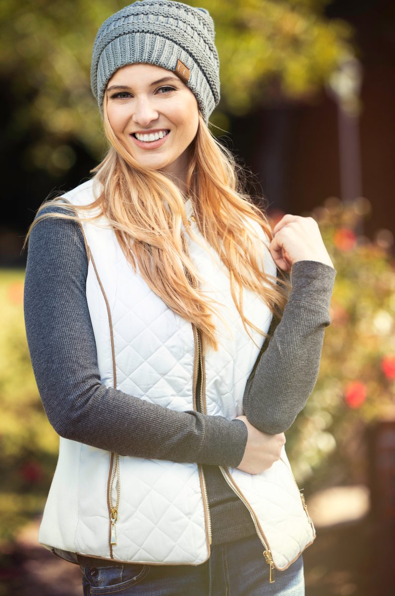 Woman in a gray quilted vest and knit beanie, smiling outdoors