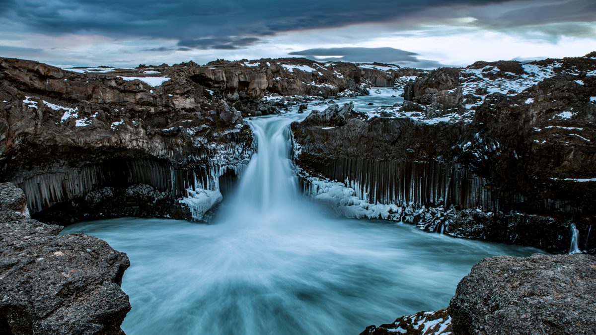 Icelandic waterfall cascading over dark basalt columns into a pool below