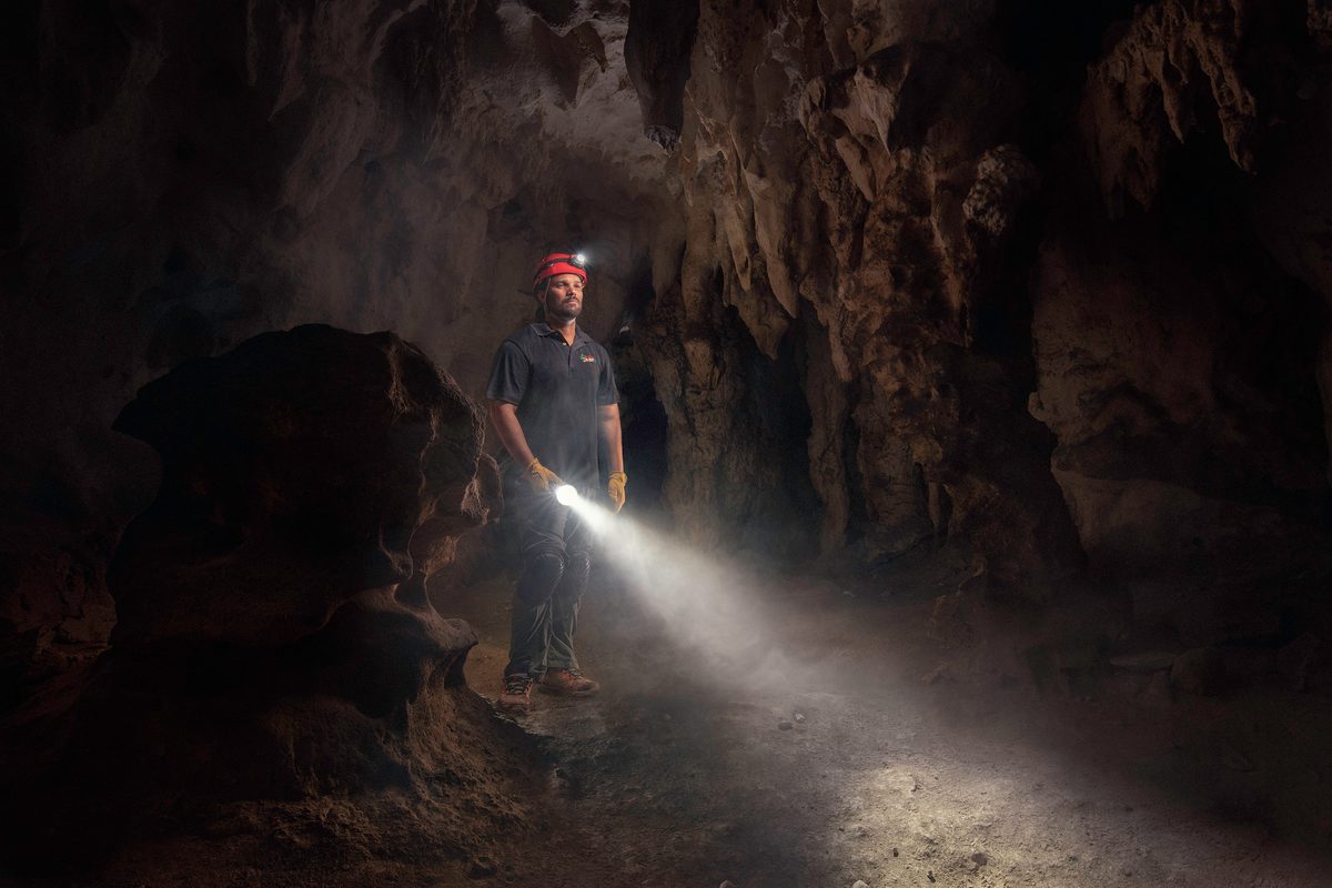 Man exploring a cave with a headlamp, beam of light cutting through the darkness