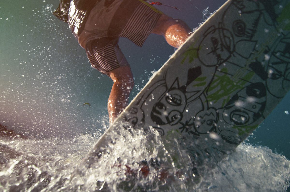 Surfer riding through breaking whitewater on a graffiti-painted board