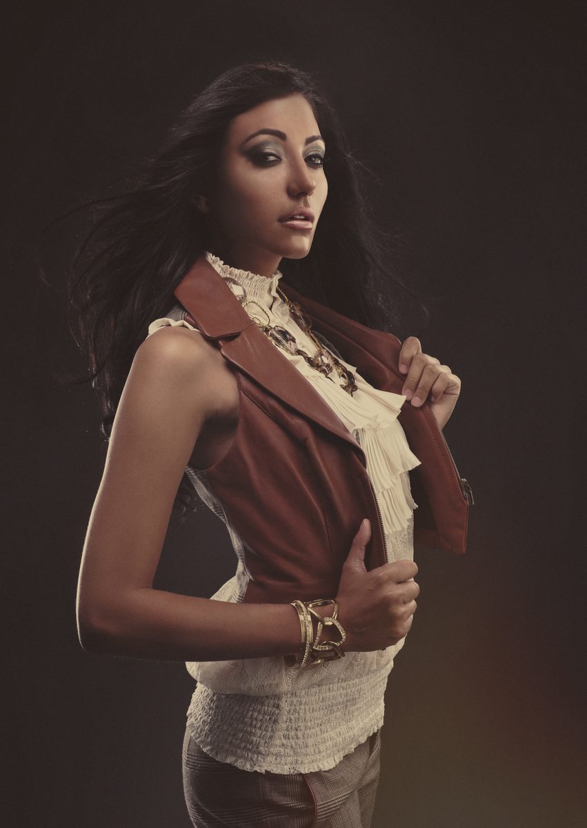 Woman in a rust and cream sleeveless top, hand at her collar, studio portrait