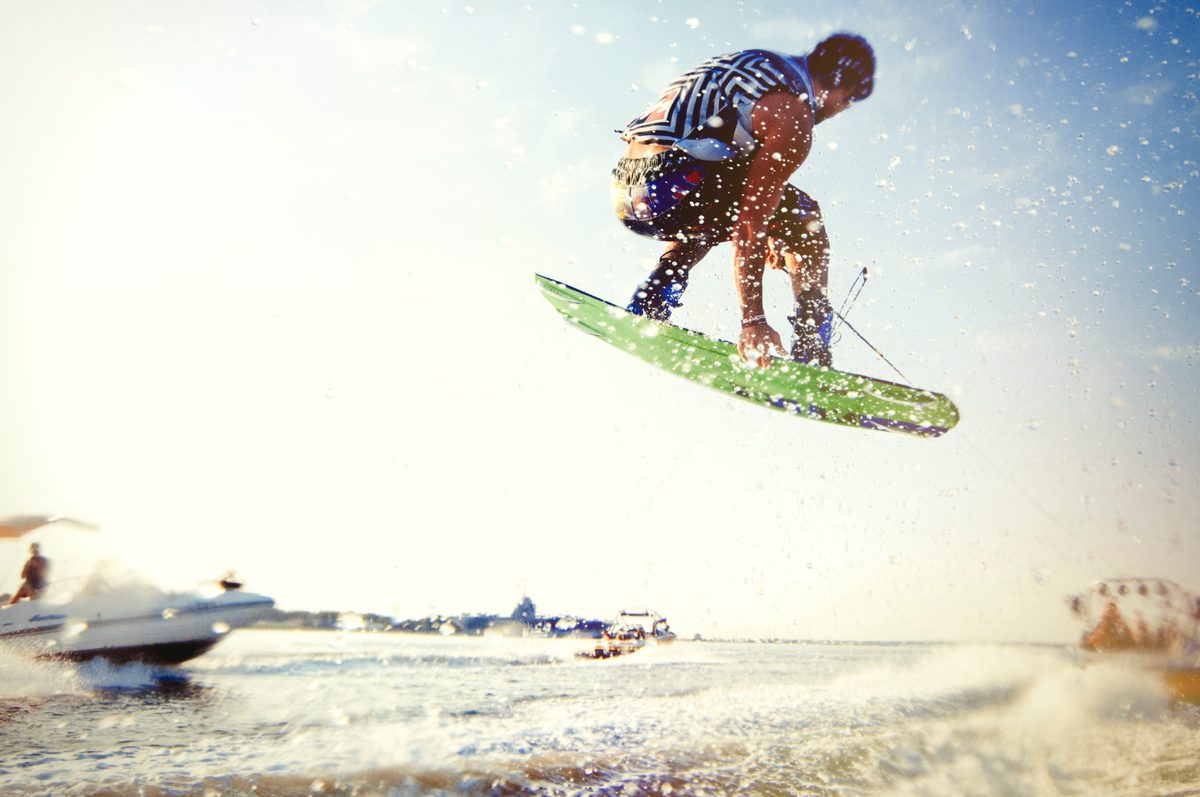 Wakeboarder jumping above the wake behind a boat, blue sky and water spray