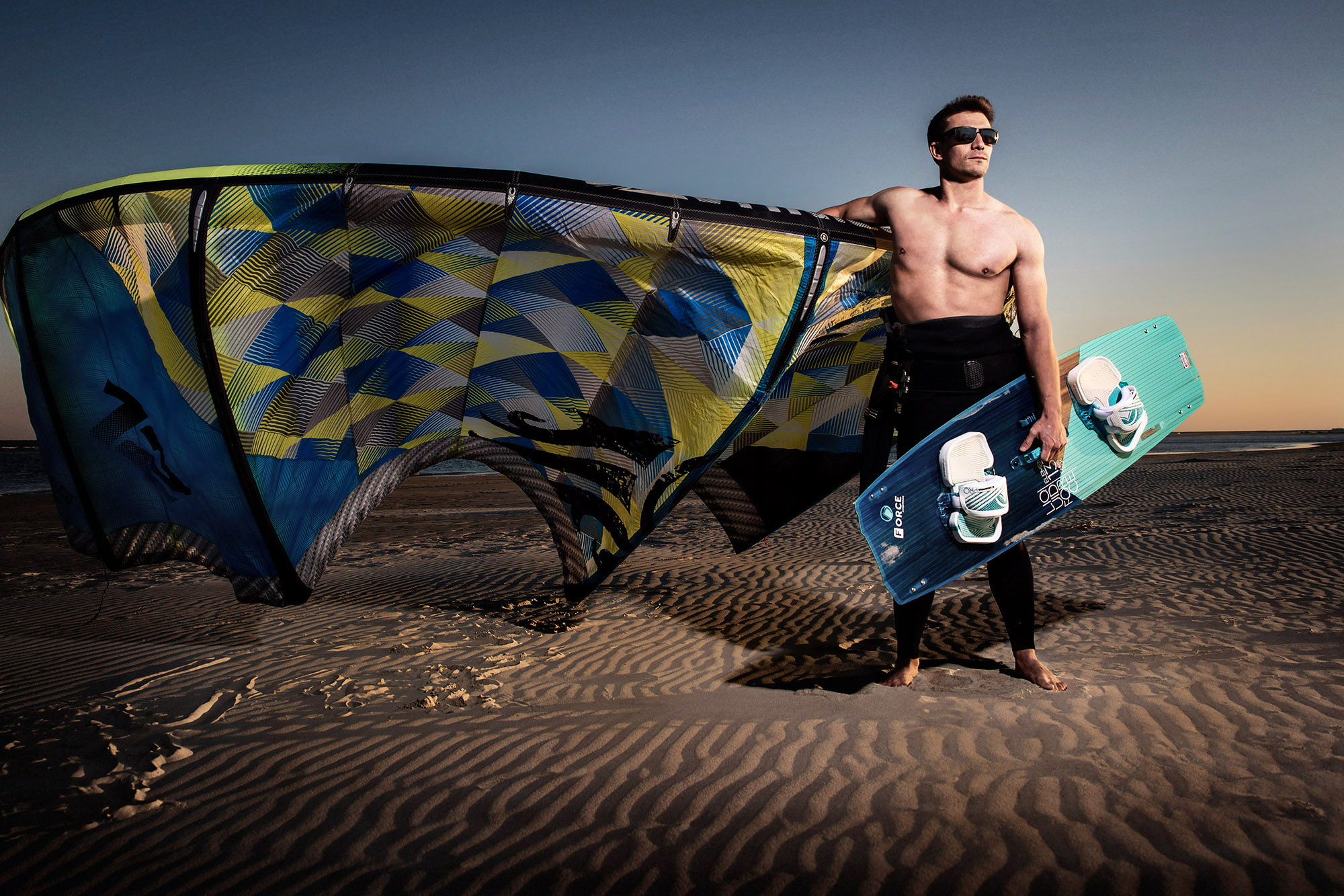 Man standing on a sand dune holding a kite and a wakeboard
