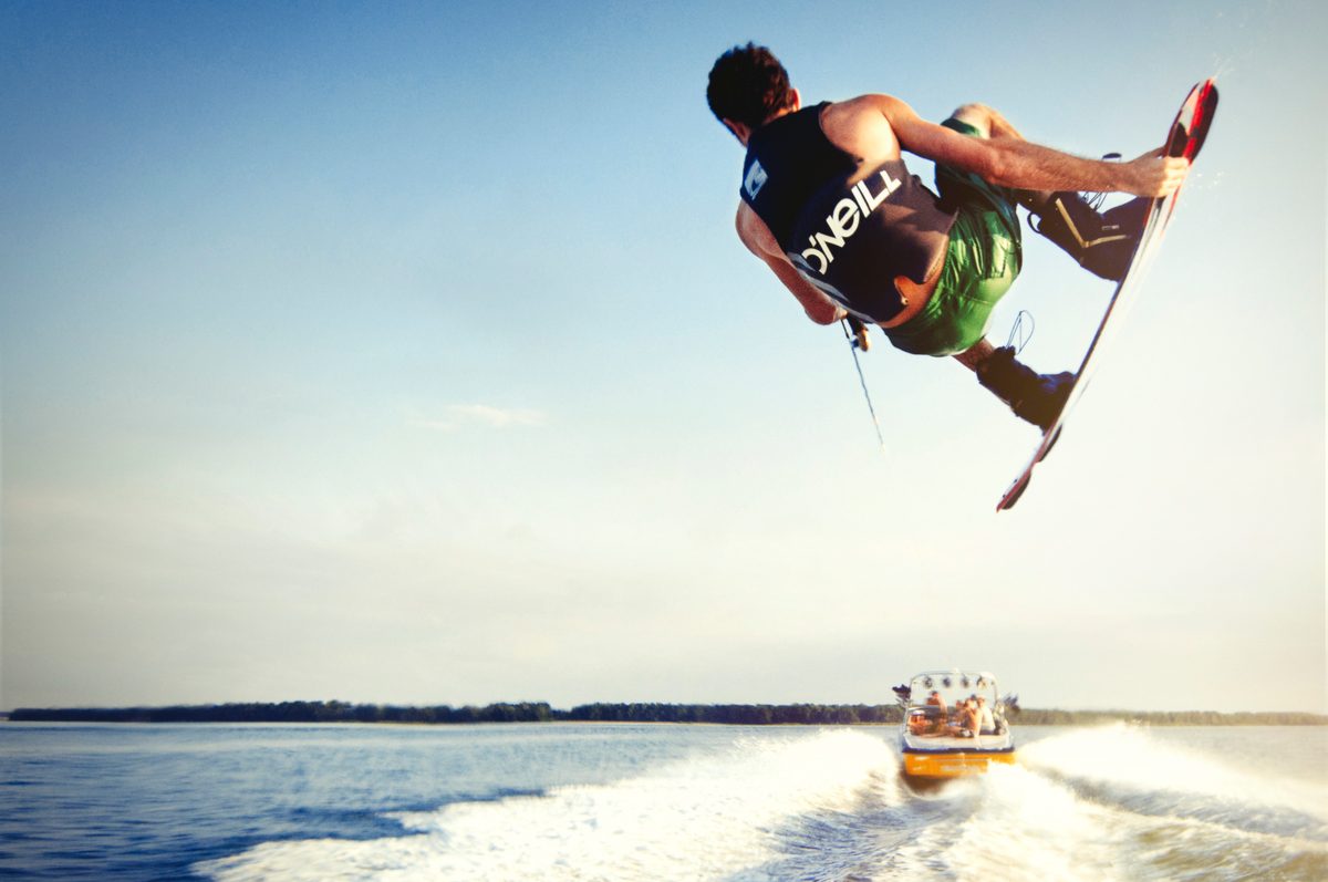 Kiteboarder jumping over a boat wake on open water under a blue sky