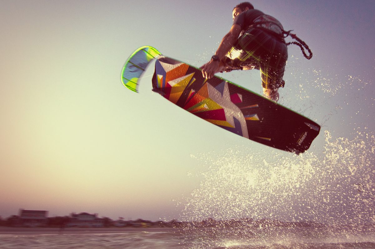 Kiteboarder airborne against a purple and pink dusk sky, kite lines visible