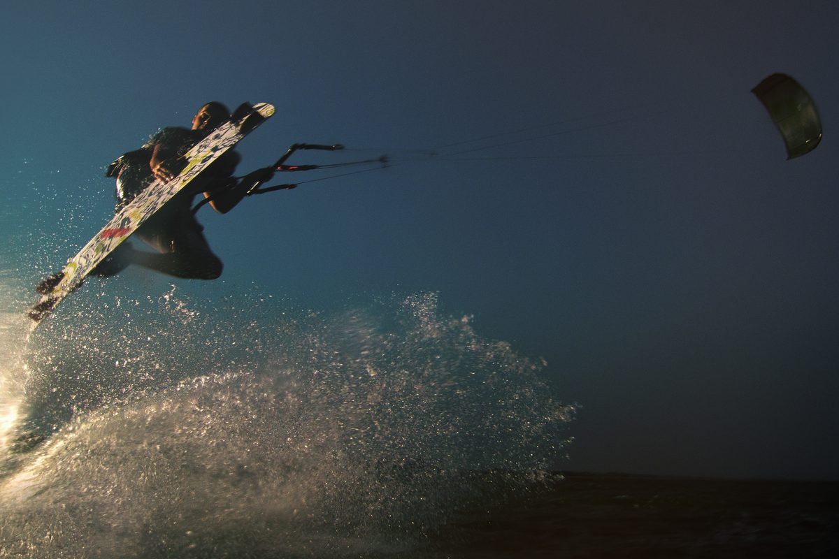Kiteboarder flipping upside down against a gray, stormy sky