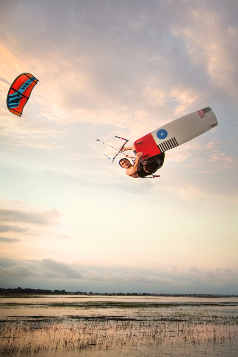 Kiteboarder silhouetted in flight over a marsh at dusk