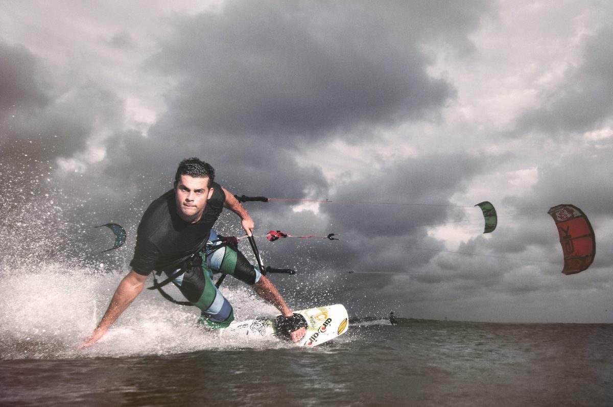 Kiteboarder cutting across the water under a stormy, cloud-filled sky