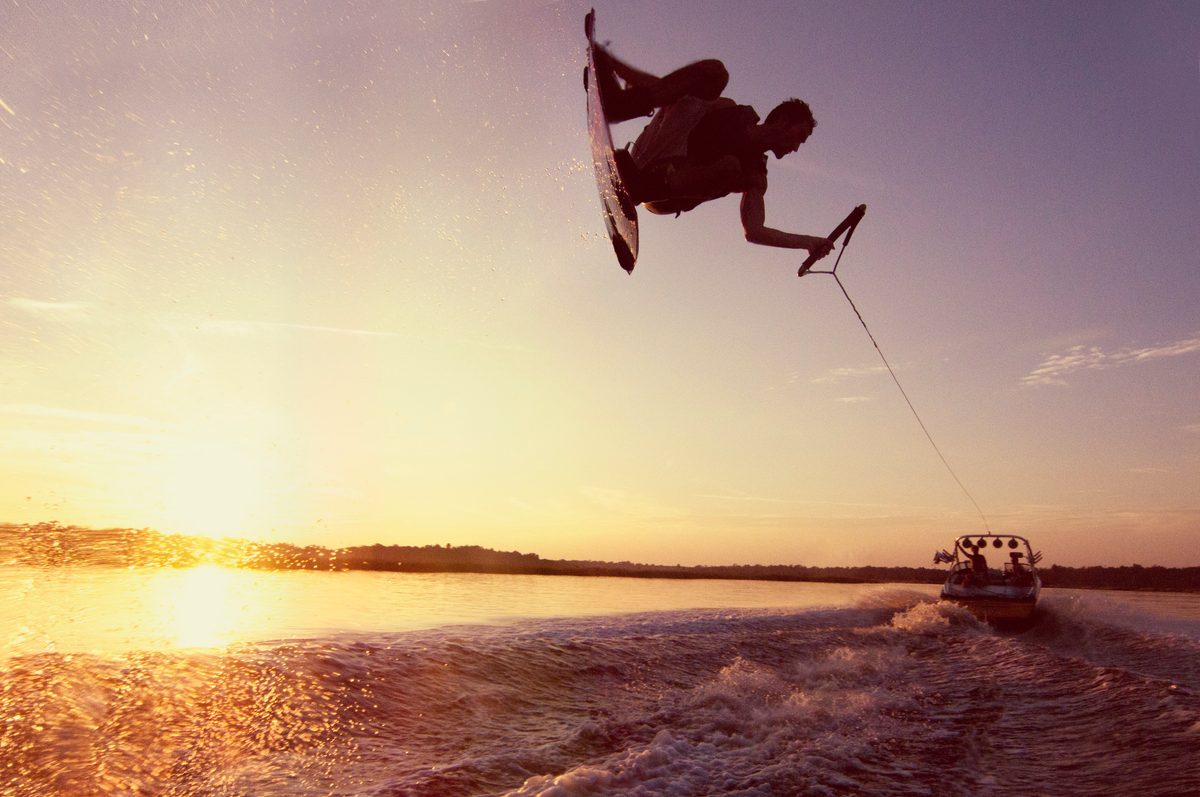 Wakeboarder airborne in silhouette at sunset, boat towing him across the water