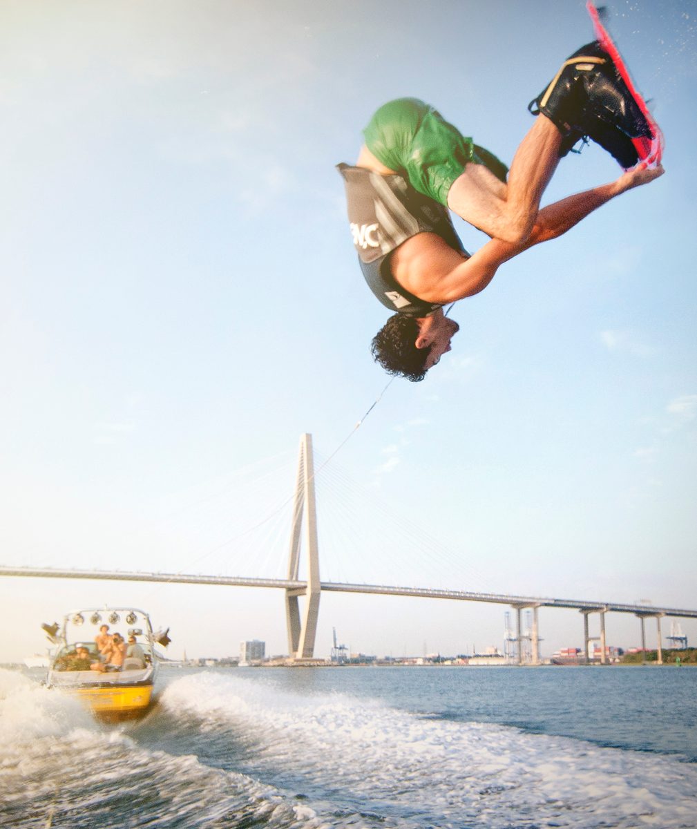 Wakeboarder flipping upside down with a large cable-stayed bridge visible in the background
