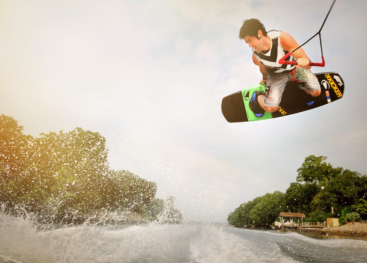 Wakeboarder jumping above the water holding the tow rope handle, trees lining the shoreline